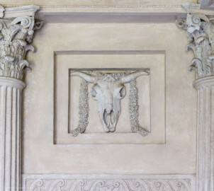 Schloss und Schlossgarten Schwetzingen - Garten - Minervatempel - Von innen - Rückwand, oben rechts - Blick auf ein zweifach abgestuftes Feld, darin ein Bukranion mit einer Girlande über den Hörnern (Gesamter Bau: Breite ca. 7 Meter, Länge ca. 9 Meter, Innenraum kubisch; Rückseite zweigeschossig mit Kellerraum; Architekt: Nicolas de Pigage (1723-1796); Bauzeit: vermutlich zwischen 1767/68 und 1773) (aufgenommen im Mai 2023, am Nachmittag) Schloss und Schlossgarten Schwetzingen - Garten - Minervatempel - Von innen - Rückwand, oben rechts - Blick auf ein zweifach abgestuftes Feld, darin ein Bukranion mit einer Girlande über den Hörnern (Gesamter Bau: Breite ca. 7 Meter, Länge ca. 9 Meter, Innenraum kubisch; Rückseite zweigeschossig mit Kellerraum; Architekt: Nicolas de Pigage (1723-1796); Bauzeit: vermutlich zwischen 1767/68 und 1773) (aufgenommen im Mai 2023, am Nachmittag)
