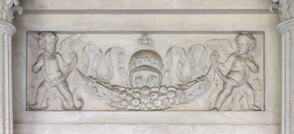 Schloss und Schlossgarten Schwetzingen - Garten - Minervatempel - Von innen - Rückwand, Feld oben in der Mitte, unterhalb der Kapitelle - Blick auf ein Relieffeld mit einer Darstellung zweier geflügelter Putti, eine Früchtegirlande haltend, darüber ein Helm mit einer Eule (Gesamter Bau: Breite ca. 7 Meter, Länge ca. 9 Meter, Innenraum kubisch; Rückseite zweigeschossig mit Kellerraum; Architekt: Nicolas de Pigage (1723-1796); Bauzeit: vermutlich zwischen 1767/68 und 1773) (aufgenommen im Mai 2023, am Nachmittag) Schloss und Schlossgarten Schwetzingen - Garten - Minervatempel - Von innen - Rückwand, Feld oben in der Mitte, unterhalb der Kapitelle - Blick auf ein Relieffeld mit einer Darstellung zweier geflügelter Putti, eine Früchtegirlande haltend, darüber ein Helm mit einer Eule (Gesamter Bau: Breite ca. 7 Meter, Länge ca. 9 Meter, Innenraum kubisch; Rückseite zweigeschossig mit Kellerraum; Architekt: Nicolas de Pigage (1723-1796); Bauzeit: vermutlich zwischen 1767/68 und 1773) (aufgenommen im Mai 2023, am Nachmittag)