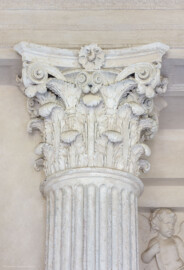 Schloss und Schlossgarten Schwetzingen - Garten - Minervatempel - Von innen - Rechte Wand, links der Mitte, Kapitellzone - Blick auf ein korinthisches Kapitell; rechts unten ein Putto des Relieffeldes (Gesamter Bau: Breite ca. 7 Meter, Länge ca. 9 Meter, Innenraum kubisch; Rückseite zweigeschossig mit Kellerraum; Architekt: Nicolas de Pigage (1723-1796); Bauzeit: vermutlich zwischen 1767/68 und 1773) (aufgenommen im Mai 2023, am späten Nachmittag)