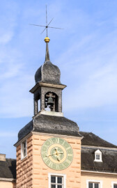 Schloss und Schlossgarten Schwetzingen - Schloss - Mittelbau - Südturm - Hofseite - Von Südost - Blick vom Ehrenhof nach oben auf das Dach des südlichen Mittelbaus und auf den Südturm, auf das Ziffernblatt der Uhr, die Turmhaube, den Glockenstuhl mit den beiden Uhrschlagglocken, den Turmknopf und auf den Hemmerschen Fünfspitz (Glockengießer: Johann und Andreas Schneidewind / Frankfurt am Main, Gussjahr: 1724; größere / kleinere Glocke: östlich / westlich, Durchmesser 68 cm / 55 cm, Nominal/Schlagton: d'' / f'') (Zifferblatt und alte Turmuhr im Südturm geschaffen 1763 vom Uhrmacher Johann Jacob Möllinger (1695-1763); alte Turmuhr genutzt bis 1968; diese trieb die Zeiger an allen drei Uhren des Schlosses an) (Mittelbau: Länge Westseite ca. 45 Meter, Breite Süd-/Nordseite ca. 38 Meter; Wiederaufbau / Erweiterung: 1698-1717; Architekt: Johann Adam Breunig) (aufgenommen im Mai 2023, am Vormittag)