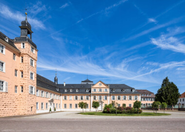 Schloss und Schlossgarten Schwetzingen - Schloss - Nordflügel / Hofkavaliersflügel - Von Süden - Blick vom Ehrenhof nach Norden auf den Ehrenhof, den Mittelbau und den Nordflügel (den Hofkavaliersflügel, heute vom Finanzamt genutzt); v.l.n.r.: nördliches Treppenhaus, Nordturm, Querbau des Nordflügels mit der Schlosskapelle, Längsbau des Nordflügels; im Hintergrund oben das Dach des Oberen Wasserwerks (NordFlügel: L-förmig, Länge x Breite Längsbau ca. 50 x 14 Meter, Querbau ca. 15 x 12 Meter; Architekt: Johann Adam Breunig (1660-1727); Fertigstellung: 1710) (aufgenommen im Mai 2023, am späten Vormittag)