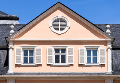 Schloss und Schlossgarten Schwetzingen - Schloss - Nordflügel / Hofkavaliersflügel - Längsbau - Mittelrisalit - Von Süden - Blick vom Ehrenhof nach Norden auf das Giebelfeld mit dem Ochsenauge und auf das Dachgeschoss des Mittelrisalits des Nordflügels; links der Mitte oben im Hintergrund das Dach des Oberen Wasserwerks (NordFlügel: L-förmig, Länge x Breite Längsbau ca. 50 x 14 Meter, Querbau ca. 15 x 12 Meter; Architekt: Johann Adam Breunig (1660-1727); Fertigstellung: 1710) (aufgenommen im Mai 2023, am frühen Nachmittag)