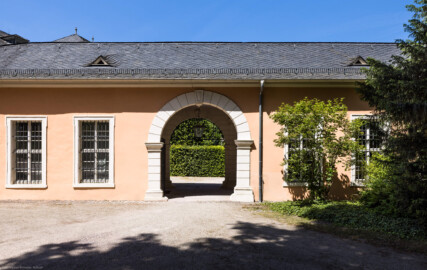 Schloss und Schlossgarten Schwetzingen - Schloss - Verbindungsbau Küchenbau-Zirkelbau / Alte Galerie - Südfassade, westliche Seite - Von Süden - Blick auf die Südfassade des Verbindungsgangs zwischen dem Küchenflügel und dem Südlichen Zirkelbau; in der Mitte der Durchgang vom Seepferdgarten zur Schlossterrasse; oben im Torbogen des Durchgangs eine Maske  (Verbindungsbau: Länge ca. 45 Meter, Breite ca. 8 Meter; Bauzeit: wohl um 1724; Architekt: unklar, evtl. Alessandro Galli da Bibiena (1686-1748) oder Johann Adam Breunig (1660-1727)) (aufgenommen im Mai 2023, am Nachmittag)