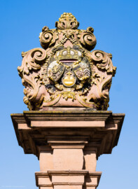 Schloss und Schlossgarten Schwetzingen - Schloss - Ehrenhof / Cour d'honneur - Eingangstor, linker / südlicher Torpfosten - Von Osten - Blick nach oben auf das Wappen von Kurfürst Johann Wilhelm (1658-1716, reg. 1690-1716); Bildhauer: Joseph Mauchert, Datierung: um 1713; ursprünglicher Aufstellungsort des Torpfostens mit dem Wappen: hinter der Brücke, um 1748 bei der Anlage des Marktplatzes vor der Brücke aufgestellt (aufgenommen im Juni 2023, am Vormittag)