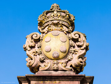 Schloss und Schlossgarten Schwetzingen - Schloss - Ehrenhof / Cour d'honneur - Eingangstor, rechter / nördlicher Torpfosten - Von Osten - Blick nach oben auf das Wappen von Anna Maria Luisa de’ Medici (1667–1743), zweite Ehefrau (Heirat 1691) des Kurfürsten Johann Wilhelm (1658-1716, reg. 1690-1716); Bildhauer: Joseph Mauchert, Datierung: um 1713; ursprünglicher Aufstellungsort des Torpfostens mit dem Wappen: hinter der Brücke, um 1748 bei der Anlage des Marktplatzes vor der Brücke aufgestellt (aufgenommen im Juni 2023, am Vormittag)