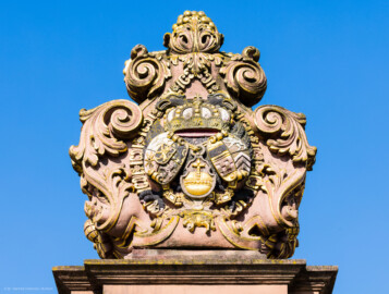 Schloss und Schlossgarten Schwetzingen - Schloss - Ehrenhof / Cour d'honneur - Eingangstor, linker / südlicher Torpfosten - Von Osten - Blick nach oben auf das Wappen von Kurfürst Johann Wilhelm (1658-1716, reg. 1690-1716); Bildhauer: Joseph Mauchert, Datierung: um 1713; ursprünglicher Aufstellungsort des Torpfostens mit dem Wappen: hinter der Brücke, um 1748 bei der Anlage des Marktplatzes vor der Brücke aufgestellt (aufgenommen im Juni 2023, am Vormittag)