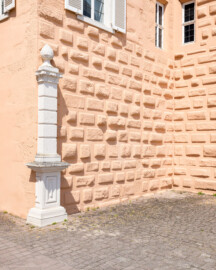 Schloss und Schlossgarten Schwetzingen - Schloss - Mittelbau - Hofseite - Von Südost - Blick auf den (später versetzten) nördlichen Torpfosten (links) des ehemaligen inneren Eingangsgitters sowie auf die Quader des Nordturms (rechts) (Mittelbau: Länge Westseite ca. 45 Meter, Breite Süd-/Nordseite ca. 38 Meter; Wiederaufbau / Erweiterung: 1698-1717; Architekten: Johann Adam Breunig, Simon Sarto) (aufgenommen im Juni 2023, um die Mittagszeit)