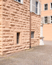 Schloss und Schlossgarten Schwetzingen - Schloss - Mittelbau - Hofseite - Von Südost - Blick auf die Quader des Südturms (den alten Bergfried der ehemaligen Wasserburg, links) und auf den (später versetzten) südlichen Torpfosten (rechts) des ehemaligen inneren Eingangsgitters (Mittelbau: Länge Westseite ca. 45 Meter, Breite Süd-/Nordseite ca. 38 Meter; Wiederaufbau / Erweiterung: 1698-1717; Architekten: Johann Adam Breunig, Simon Sarto) (aufgenommen im Juni 2023, um die Mittagszeit)