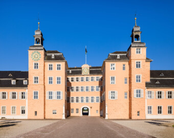 Schloss und Schlossgarten Schwetzingen - Schloss - Mittelbau - Hofseite - Von Osten - Zentraler Blick vom Ehrenhof nach Westen auf den Mittelbau mit dem Süd- und Nordturm und der Durchfahrt in den Garten sowie auf die Ansätze des Süd- und Nordflügels; die Ostwand des mittleren zurückgesetzten Teils des Mittelbaus (mit der Durchfahrt) verläuft nicht parallel zur Front des Mittelbaus (Mittelbau: Länge Westseite ca. 45 Meter, Breite Süd-/Nordseite ca. 38 Meter; Wiederaufbau / Erweiterung: 1698-1717; Architekt: Johann Adam Breunig) (aufgenommen im Juli 2023, am frühen Vormittag)