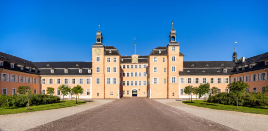 Schloss und Schlossgarten Schwetzingen - Schloss - Ostseite / Mittelbau / Süd- und Nordflügel / Ehrenhof - Von Osten - Zentraler Blick vom Ehrenhof nach Westen auf den Mittelbau mit dem Süd- und Nordturm und der Durchfahrt in den Garten sowie auf den Südflügel / Hofkavaliersflügel (links) und den Nordflügel / Hofdamenflügel (rechts) (Mittelbau und Flügel: Wiederaufbau / Erweiterung: 1698-1717; Architekten: Johann Adam Breunig, Simon Sarto) (aufgenommen im Juli 2023, am frühen Vormittag)