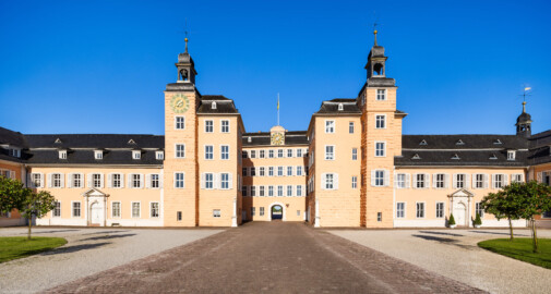 Schloss und Schlossgarten Schwetzingen - Schloss - Ostseite / Mittelbau / Süd- und Nordflügel / Ehrenhof - Von Osten - Zentraler Blick vom Ehrenhof nach Westen auf den Mittelbau mit dem Süd- und Nordturm und der Durchfahrt in den Garten sowie auf den Südflügel / Hofkavaliersflügel (links) und den Nordflügel / Hofdamenflügel (rechts) (Mittelbau und Flügel: Wiederaufbau / Erweiterung: 1698-1717; Architekten: Johann Adam Breunig, Simon Sarto) (aufgenommen im Juli 2023, am Vormittag)