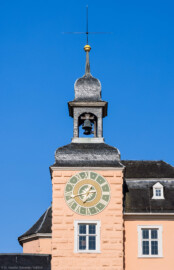Schloss und Schlossgarten Schwetzingen - Schloss - Mittelbau - Südturm - Hofseite - Von Osten - Blick vom Ehrenhof nach oben auf die Ostfassaden des südlichen Mittelbaus und des Südturms, auf das Ziffernblatt der Uhr, die Turmhaube, den Glockenstuhl mit den beiden Uhrschlagglocken, den Turmknopf und auf den Hemmerschen Fünfspitz (Glockengießer: Johann und Andreas Schneidewind / Frankfurt am Main, Gussjahr: 1724; größere / kleinere Glocke: östlich / westlich, Durchmesser 68 cm / 55 cm, Nominal/Schlagton: d'' / f'') (Zifferblatt und alte Turmuhr im Südturm geschaffen 1763 vom Uhrmacher Johann Jacob Möllinger (1695-1763); alte Turmuhr genutzt bis 1968; diese trieb die Zeiger an allen drei Uhren des Schlosses an) (Mittelbau: Länge Westseite ca. 45 Meter, Breite Süd-/Nordseite ca. 38 Meter; Wiederaufbau / Erweiterung: 1698-1717; Architekt: Johann Adam Breunig) (aufgenommen im Juli 2023, am Vormittag)