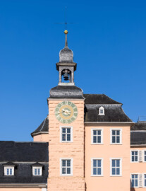 Schloss und Schlossgarten Schwetzingen - Schloss - Mittelbau - Südturm - Hofseite - Von Osten - Blick vom Ehrenhof nach oben auf die Ostfassaden des südlichen Mittelbaus und des Südturms, auf das Ziffernblatt der Uhr, die Turmhaube, den Glockenstuhl mit den beiden Uhrschlagglocken, den Turmknopf und auf den Hemmerschen Fünfspitz (Glockengießer: Johann und Andreas Schneidewind / Frankfurt am Main, Gussjahr: 1724; größere / kleinere Glocke: östlich / westlich, Durchmesser 68 cm / 55 cm, Nominal/Schlagton: d'' / f'') (Zifferblatt und alte Turmuhr im Südturm geschaffen 1763 vom Uhrmacher Johann Jacob Möllinger (1695-1763); alte Turmuhr genutzt bis 1968; diese trieb die Zeiger an allen drei Uhren des Schlosses an) (Mittelbau: Länge Westseite ca. 45 Meter, Breite Süd-/Nordseite ca. 38 Meter; Wiederaufbau / Erweiterung: 1698-1717; Architekt: Johann Adam Breunig) (aufgenommen im Juli 2023, am Vormittag)