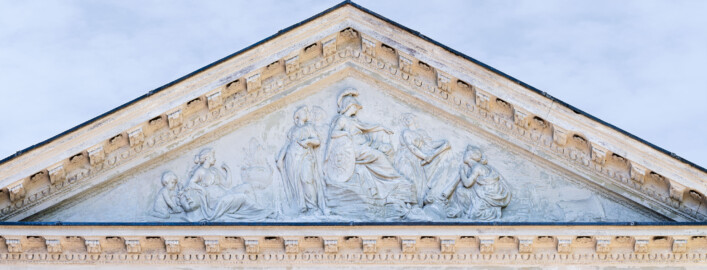 Schloss und Schlossgarten Schwetzingen - Garten - Minervatempel - Tympanon - Von aussen - Vorderseite - Von Nordost - Reliefdarstellung der Göttin Minerva als Beschützerin der Gartenkunst; Relief geschaffen 1769 von Franz Conrad Linck (1730-1793), nach einer Vorlage von Peter Anton von Verschaffelt (1710-1793) am Bibliotheksbau von Schloss Mannheim; in der Mitte: Minerva, auf einem Steinhaufen sitzend, mit Helm und Schild, auf eine Papierrolle zeigend; rechts: zwei Frauen, die Papierrolle haltend; ganz rechts: ein Fels mit einem Wasserquelle; links: zwei Frauen, eine mit Sichel und Spaten; links davon: eine weitere Frau, sitzend, den Arm auf einen Steinkopf stützend; ganz links: ein Putto mit Hammer und Meisel, den Stein  bearbeitend (aufgenommen im Juli 2023, um die Mittagszeit)