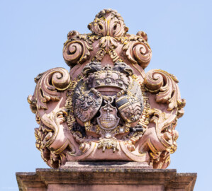Schloss und Schlossgarten Schwetzingen - Schloss - Ehrenhof / Cour d'honneur - Eingangstor, linker / nördlicher Torpfosten - Von Westen - Blick nach oben auf das Wappen von Kurfürst Johann Wilhelm (1658-1716, reg. 1690-1716); Bildhauer: Joseph Mauchert, Datierung: um 1713; ursprünglicher Aufstellungsort des Torpfostens mit dem Wappen: vor / westlich der Brücke, um 1748 bei der Anlage des Marktplatzes hinter der Brücke aufgestellt (aufgenommen im Juli 2023, am frühen Nachmittag)