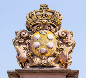Schloss und Schlossgarten Schwetzingen - Schloss - Ehrenhof / Cour d'honneur - Eingangstor, rechter / südlicher Torpfosten - Von Westen - Blick nach oben auf das Wappen von Anna Maria Luisa de’ Medici (1667–1743), zweite Ehefrau (Heirat 1691) des Kurfürsten Johann Wilhelm (1658-1716, reg. 1690-1716); Bildhauer: Joseph Mauchert, Datierung: um 1713; ursprünglicher Aufstellungsort des Torpfostens mit dem Wappen: vor / westlich der Brücke, um 1748 bei der Anlage des Marktplatzes hinter der Brücke aufgestellt (aufgenommen im Juli 2023, am frühen Nachmittag)