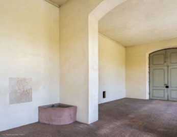 Schloss und Schlossgarten Schwetzingen - Garten - Neue Orangerie - Von innen - Östlicher Seitenflügel / Eckpavillon - Von Südwest - Blick auf die durchbrochene Trennwand zwischen dem dreizehnachsigen Seitenflügel und dem dreiachsigen ("Eck-") Pavillon, links ein Brunnen, ganz links ein freigelegtes Graffiti, rechts ein Wanddurchbruch für die Beschickung eines Ofens mit Heizmaterial von außen, ganz rechts die große Tür zum Glashaus (Gesamter Bau: Länge ca. 171 Meter, Breite ca. 10-12 Meter; Bauzeit: 1761-1762; Architekt: Nicolas de Pigage; umfangreiche Instandsetzung: 1994-1999) (aufgenommen im Juli 2023, am Nachmittag) Schloss und Schlossgarten Schwetzingen - Garten - Neue Orangerie - Von innen - Östlicher Seitenflügel / Eckpavillon - Von Südwest - Blick auf die durchbrochene Trennwand zwischen dem dreizehnachsigen Seitenflügel und dem dreiachsigen ("Eck-") Pavillon, links ein Brunnen, ganz links ein freigelegtes Graffiti, rechts ein Wanddurchbruch für die Beschickung eines Ofens mit Heizmaterial von außen, ganz rechts die große Tür zum Glashaus (Gesamter Bau: Länge ca. 171 Meter, Breite ca. 10-12 Meter; Bauzeit: 1761-1762; Architekt: Nicolas de Pigage; umfangreiche Instandsetzung: 1994-1999) (aufgenommen im Juli 2023, am Nachmittag)
