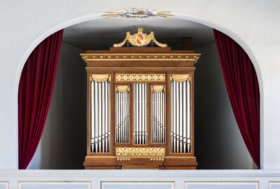Schloss und Schlossgarten Schwetzingen - Schloss - Nordflügel, Nord-Süd-Teil - Schlosskapelle - Orgelempore - Orgel - Von Süden - Blick von der Hofloge auf die Orgelempore und auf einen Teil des Orgelprospektes mit den Prospektpfeifen sowie auf das "badische" Wappen oben auf der Orgel (mit vertauschten Farben des Wappens Badens) (Orgelbauer: Andreas Ubhauser (1765-1822), Bauzeit: 1806, umfassende Restaurierung: 1980-1982, Originalteile: ca. 90 Prozent;  Windwerk: Schleifladen und elektrisches Gebläse, Register: 10, Manuale: 1 / C-f3, Pedale: 1 / C-f0; Orgelpfeifen aus Zinn, Tastatur aus Ebenholz) (aufgenommen im August 2023, am Nachmittag)