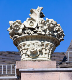 Schloss und Schlossgarten Schwetzingen - Garten - Nördlicher Zirkelbau - Östlicher Eck-Pavillon - Von Westen - Blick nach oben auf den nördlichen (linken) Blumenkorb mit Blumen; Kopie, Original der Skulptur vermutlich gehauen von Johann Matthäus van den Branden (1716-1788) (Gesamter Bau: Länge Bogen ca. 175 Meter, Breite zwischen ca. 11 und 18 Meter, 51 Achsen, 5 Pavillons, 4 Zwischenbauten; Architekt: Alessandro Alessandro Galli da Bibiena (1686-1748), Bauleitung: zuerst Guillaume d’Hauberat (1680–1749), dann Nicolas de Pigage (1723-1796); Bauzeit: 1748-1750) (aufgenommen im August 2023, am späten Nachmittag)