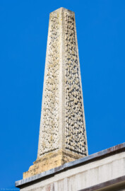 Schloss und Schlossgarten Schwetzingen - Garten - Badhaus - Von aussen - Westseite - Obelisk, Nordwestecke - Von Südwest - Blick nach oben auf den Obelisken oberhalb der Attikabrüstung in der nordwestlichen Ecke des Badhauses; Obelisk mit geböschtem Sockel, sehr flacher Spitze, mit Tropfen aus Stuck (Gesamter Bau: Länge x Breite ca. 18 x 14 Meter, Höhe ca. 10 Meter; Architekt: Nicolas de Pigage (1723-1796); Bauzeit: 1768-1772; Gesamtinstandsetzung innen und außen: 1999-2006) (aufgenommen im August 2023, am späten Nachmittag)