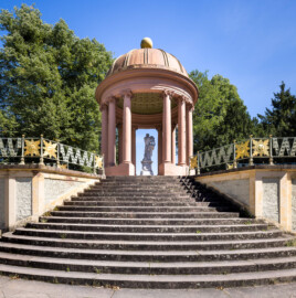 Schloss und Schlossgarten Schwetzingen - Garten - Anlage Apollotempel - Von außen - Von Westen - Blick von der unteren Terrasse (dem Belvedere) auf die Treppe zur oberen Terrasse mit dem schmiedeeisernen Geländer mit Sonnengesichtern sowie auf den Rundtempel (Monopteros) des Apollo (mit zwölf Säulen ionischer Säulenordnung, ohne Cella), darin eine Statue des Apollo beim linkshändigen Lyra-Spiel (Skulptur geschaffen von Peter Anton von Verschaffelt, vor 1773) (Anlage: Länge x Breite: ca. 30 x 20 Meter; Bauzeit: 1762-1777; Architekt: Nicolas de Pigage) (aufgenommen im September 2023, am frühen Nachmittag)