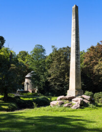 Schloss und Schlossgarten Schwetzingen - Garten - Obelisk, Nähe Römischem Wasserkastell - Von Nordost - Blick vom östlichen Aquädukt auf den Obelisken, im Hintergrund der Tempel der Botanik; der Obelisk dient als Denkmal für die in einer angenommenen Schlacht zwischen Römern und Germanen Gefallenen; die Skulptur markiert den Fundort von römisch-germanischen Gräbern, entdeckt 1777 bei Erdarbeiten zur Anlage des Arboretums (Obelisk: Höhe: ca. ? Meter; Bauzeit: 1779; Architekt: Nicolas de Pigage) (aufgenommen im September 2023, um die Mittagszeit)