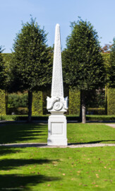 Schloss und Schlossgarten Schwetzingen - Garten - Kreisparterre, nordöstliches Rasenfeld - Nordöstlicher Obelisk - Von Süden - Blick auf die Südseite des Obelisken (Bildhauer: Peter Anton von Verschaffelt (1710-1793); Datierung: 1762-69; Obelisk Teil einer Vierergruppe im Kreisparterre; Material: roter Sandstein (Medaillons aus gelbem Sandstein); Fassung: Weiß; Obelisk dreigeteilt; Sockel, Block mit Medaillonbildnissen, eigentlicher Obelisk; Abmessungen: Höhe ca. 6 Meter, Sockel Höhe 155 cm / Breite 87 cm, Block mit Medaillons Höhe 67 cm / Breite 87 cm; Obelisk oben mit Tropfsteindekor) (aufgenommen im September 2023, am Nachmittag)