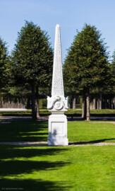 Schloss und Schlossgarten Schwetzingen - Garten - Kreisparterre, südostliches Rasenfeld - Südostlicher Obelisk - Von Süden - Blick auf die Südseite des Obelisken (Bildhauer: Peter Anton von Verschaffelt (1710-1793); Datierung: 1762-69; Obelisk Teil einer Vierergruppe im Kreisparterre; Material: roter Sandstein (Medaillons aus gelbem Sandstein); Fassung: Weiß; Obelisk dreigeteilt; Sockel, Block mit Medaillonbildnissen, eigentlicher Obelisk; Abmessungen: Höhe ca. 6 Meter, Sockel Höhe 155 cm / Breite 87 cm, Block mit Medaillons Höhe 67 cm / Breite 87 cm; Obelisk oben mit Tropfsteindekor) (aufgenommen im September 2023, am Nachmittag)