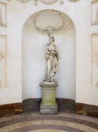 Schloss und Schlossgarten Schwetzingen - Garten - Tempel der Botanik - Von innen - Skulptur Botanik - Von Osten - Blick auf die Skulptur der Botanik, gehauen von Francesco Carabelli (1737-1798), gekauft 1775 in Italien; ursprünglich stellte die Skulptur Ceres / Demeter dar, die Göttin des Ackerbaus und der Fruchtbarkeit, die ein Ährenbündel in ihrem Arm hielt; die Skulptur wurde umgearbeitet zur Botanik, die in ihrem linken Arm ein Bündel Papiere hielt, beschriftet mit "Caroli Linnei sistema plantarum", ein Hinweis auf die beiden bedeutsamsten Werke "Species Plantarum" und "Systema Naturae" von Carl von Linné (1707-1778); heute ist das Manuskript im linken Arm nicht mehr vorhanden (Tempel: Durchmesser ca. 7 Meter; Bauzeit: 1777-1780; Architekt: Nicolas de Pigage) (aufgenommen im September 2023, um die Mittagszeit)