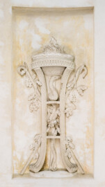Schloss und Schlossgarten Schwetzingen - Garten - Tempel der Botanik - Von innen - Unteres großes Wandfeld, Nordostseite - Blick auf ein Stuckrelief, den Winter symbolisierend mittels zweier gekreuzter Krummstäbe mit Eichenlaub; in der Mitte ein Dreifuß mit hochaufgerichteter Schlange, oben eine Schale mit brennendem Feuer; Stuckateur Joseph Anton Pozzi (1732-1811) (Tempel: Durchmesser ca. 7 Meter; Bauzeit: 1777-1780; Architekt: Nicolas de Pigage) (aufgenommen im September 2023, am späten Vormittag)