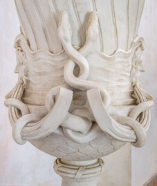 Schloss und Schlossgarten Schwetzingen - Garten - Tempel der Botanik - Von innen - Südliche Vase - Von Osten - Blick auf einen Ausschnitt der Vase; Vase unten mit Schuppen überzogen, mittig ein verschlungenes Schlangenpaar, links und rechts zwei bärtige Männerköpfe (Bildhauer Postament: Franz Conrad Linck (1730-1793), um 1779; Bildhauer Vase: unklar, evtl. Peter Anton von Verschaffelt (1710-1793), Francesco Carabelli (1737-1798) oder Franz Conrad Linck (1730-1793)) (Tempel: Durchmesser ca. 7 Meter; Bauzeit: 1777-1780; Architekt: Nicolas de Pigage) (aufgenommen im September 2023, um die Mittagszeit)