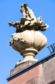 Schloss und Schlossgarten Schwetzingen - Garten - Nördlicher Zirkelbau - Östlicher Pavillon - Von Südwest - Blick nach oben auf eine Blumenvase mit Blumen an der linken / westlichen Seite des östlichen Pavillons; Kopie, Original der Skulptur vermutlich gehauen von Johann Matthäus van den Branden (1716-1788) (Gesamter Bau: Länge Bogen ca. 175 Meter, Breite zwischen ca. 11 und 18 Meter, 51 Achsen, 5 Pavillons, 4 Pavillonten; Architekt: Alessandro Alessandro Galli da Bibiena (1686-1748), Bauleitung: zuerst Guillaume d’Hauberat (1680–1749), dann Nicolas de Pigage (1723-1796); Bauzeit: 1748-1750) (aufgenommen im September 2023, am späten Vormittag)