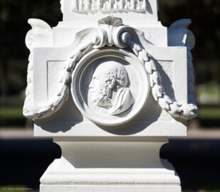 Schloss und Schlossgarten Schwetzingen - Garten - Kreisparterre, südöstliches Rasenfeld, entlang der Nord-Süd-Achse - Südöstlicher Obelisk, Ostseite - Blick auf ein männliches verwittertes Profilbildnis / Flachrelief, umgeben von einem Lorbeerfeston (Person nicht eindeutig identifizierbar) (Bildhauer: Peter Anton von Verschaffelt (1710-1793); Datierung: 1762-69; Obelisk Teil einer Vierergruppe im Kreisparterre; Material: roter Sandstein (Medaillons aus gelbem Sandstein); Fassung: Weiß; Obelisk dreigeteilt; Sockel, Block mit Medaillonbildnissen, eigentlicher Obelisk; Abmessungen: Höhe ca. 6 Meter, Sockel Höhe 155 cm / Breite 87 cm, Block mit Medaillons Höhe 67 cm / Breite 87 cm; Obelisk oben mit Tropfsteindekor) (aufgenommen im September 2023, am späten Vormittag) Schloss und Schlossgarten Schwetzingen - Garten - Kreisparterre, südöstliches Rasenfeld, entlang der Nord-Süd-Achse - Südöstlicher Obelisk, Ostseite - Blick auf ein männliches verwittertes Profilbildnis / Flachrelief, umgeben von einem Lorbeerfeston (Person nicht eindeutig identifizierbar) (Bildhauer: Peter Anton von Verschaffelt (1710-1793); Datierung: 1762-69; Obelisk Teil einer Vierergruppe im Kreisparterre; Material: roter Sandstein (Medaillons aus gelbem Sandstein); Fassung: Weiß; Obelisk dreigeteilt; Sockel, Block mit Medaillonbildnissen, eigentlicher Obelisk; Abmessungen: Höhe ca. 6 Meter, Sockel Höhe 155 cm / Breite 87 cm, Block mit Medaillons Höhe 67 cm / Breite 87 cm; Obelisk oben mit Tropfsteindekor) (aufgenommen im September 2023, am späten Vormittag)