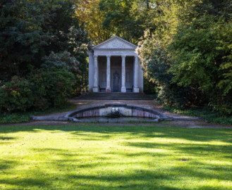 Schloss und Schlossgarten Schwetzingen - Garten - Minervatempel - Von aussen - Vorderseite - Von Nordost - Blick auf den Tritonenbrunnen mit den beiden Putti und auf den Minervatempel mit (von unten nach oben) fünfstufiger Krepis, vier Säulen korinthischen Ordnung auf Plinthen, Gebälk (mit Architrav und Fries) und dreieckigem Giebelfeld mit Reliefdarstellung  (Gesamter Bau: Breite ca. 7 Meter, Länge ca. 9 Meter, Innenraum kubisch; Rückseite zweigeschossig mit Kellerraum; Architekt: Nicolas de Pigage (1723-1796); Bauzeit: vermutlich zwischen 1767/68 und 1773) (aufgenommen im September 2023, am späten Vormittag)