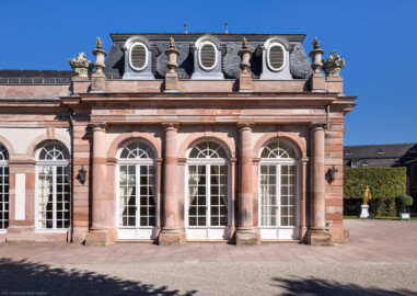 Schloss und Schlossgarten Schwetzingen - Garten - Nördlicher Zirkelbau - Östlicher Eck-Pavillon - Von Südwest - Blick auf den dreiachsigen Eck-Pavillon, die drei großen Türen, die vier toskanischen Säulen, das Gebälk und den Schmuck (Vasen und Blumenkörbe) (Gesamter Bau: Länge Bogen ca. 175 Meter, Breite zwischen ca. 11 und 18 Meter, 51 Achsen, 5 Pavillons, 4 Zwischenbauten; Architekt: Alessandro Alessandro Galli da Bibiena (1686-1748), Bauleitung: zuerst Guillaume d’Hauberat (1680–1749), dann Nicolas de Pigage (1723-1796); Bauzeit: 1748-1750) (aufgenommen im September 2023, am Nachmittag)
