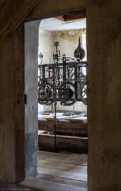 Schloss und Schlossgarten Schwetzingen - Schloss - Mittelbau - Von innen - Dachstuhl, Südseite - Uhrenstube im südlichen Turm - Von Nordwest - Blick vom Dachzimmer nördlich der Uhrenstube in die Uhrenstube des südlichen Turms; in der Mitte des Raums die alte große Schlossuhr von Johann Jacob Möllinger (1695-1763) mit Viertel- und Stundenschlag, stillgelegt seit 1968; die umlaufende Inschrift am oberen Rahmen der Turmuhr lautet: "AUF HOHEN CHURFÜRSTLICHEN BEFEHL WURDE DIESES WERCK VON IACOB MOELLINGER IN NEUSTATT VERFERTIGET Ao. 1763"; diese Uhr  bewegte gleichzeitig vermittels einer Hebelübersetzung die Zeiger an den Uhren des Südturms, der Ost- sowie der Westfassade des Mittelbaus; die Zifferblätter der drei Uhren sind ebenso von Johann Jacob Möllinger gefertigt (Mittelbau: Länge Westseite ca. 45 Meter, Breite Süd-/Nordseite ca. 38 Meter; Wiederaufbau / Erweiterung: 1698-1717; Architekten: Johann Adam Breunig, Simon Sarto) (aufgenommen im Oktober 2023, am Nachmittag)