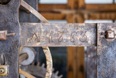 Schloss und Schlossgarten Schwetzingen - Schloss - Mittelbau - Von innen - Dachstuhl, Südseite - Uhrenstube im südlichen Turm - Von Norden - Blick auf die Inschrift "Ao. 1763" am hinteren / nördlichen oberen Rahmen der großen alten Schlossuhr von Johann Jacob Möllinger (1695-1763) mit Viertel- und Stundenschlag, stillgelegt 1968; die gesamte umlaufende Inschrift am oberen Rahmen der Turmuhr lautet: "AUF HOHEN CHURFÜRSTLICHEN BEFEHL WURDE DIESES WERCK VON IACOB MOELLINGER IN NEUSTATT VERFERTIGET Ao. 1763" (Mittelbau: Länge Westseite ca. 45 Meter, Breite Süd-/Nordseite ca. 38 Meter; Wiederaufbau / Erweiterung: 1698-1717; Architekten: Johann Adam Breunig, Simon Sarto) (aufgenommen im November 2023, am Nachmittag) Schloss und Schlossgarten Schwetzingen - Schloss - Mittelbau - Von innen - Dachstuhl, Südseite - Uhrenstube im südlichen Turm - Von Norden - Blick auf die Inschrift "Ao. 1763" am hinteren / nördlichen oberen Rahmen der großen alten Schlossuhr von Johann Jacob Möllinger (1695-1763) mit Viertel- und Stundenschlag, stillgelegt 1968; die gesamte umlaufende Inschrift am oberen Rahmen der Turmuhr lautet: "AUF HOHEN CHURFÜRSTLICHEN BEFEHL WURDE DIESES WERCK VON IACOB MOELLINGER IN NEUSTATT VERFERTIGET Ao. 1763" (Mittelbau: Länge Westseite ca. 45 Meter, Breite Süd-/Nordseite ca. 38 Meter; Wiederaufbau / Erweiterung: 1698-1717; Architekten: Johann Adam Breunig, Simon Sarto) (aufgenommen im November 2023, am Nachmittag)