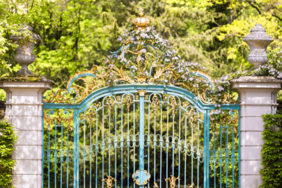 Schloss und Schlossgarten Schwetzingen - Garten - Arboretum - Südliches Tor - Von Süden - Blick auf das schmiedeeiserne, teilvergoldete Prachttor, der südliche Eingang zum Arboretum, mit Rokoko-Verzierungen, oben das Monogramm "CT" (Carl Theodor) und ganz oben die Krone (Eisentür fertiggestellt 1755; entworfen von Franz Wilhelm Rabaliatti, geschmiedet von den Mannheimer Schlossermeistern Strickling und Frockmann; ursprünglich an einem anderen Ort verbaut) (aufgenommen im April 2024, am frühen Nachmittag)
