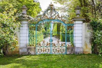 Schloss und Schlossgarten Schwetzingen - Garten - Arboretum - Südliches Tor - Von Norden - Blick auf das schmiedeeiserne, teilvergoldete Prachttor, der südliche Eingang zum Arboretum, mit Rokoko-Verzierungen, oben das Monogramm "CT" (Carl Theodor) und ganz oben die Krone (Eisentür fertiggestellt 1755; entworfen von Franz Wilhelm Rabaliatti, geschmiedet von den Mannheimer Schlossermeistern Strickling und Frockmann; ursprünglich an einem anderen Ort verbaut) (aufgenommen im April 2024, am frühen Nachmittag)