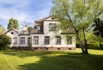Schloss und Schlossgarten Schwetzingen - Sonstige Bauten im / Nähe Garten - Hofgärtnerhaus, südlich Baumagazin - Von außen - Von Nordwest - Blick auf die Nordseite des Hofgärtnerhauses (rechte 4 Fenster im Erdgeschoss) und des Verbindungsbaus (linke 4 Fenster im Erdgeschoss); erster Bewohner war Gustav Adolf Unselt (1866-1924), Hofgärtner und Gartendirektor 1899-1924, auch Spargelpionier und Züchter ertragreicher Spargelsorten (Architekt: Großherzogliche Generalinstanz; Bauleitung: Großherzogliches Hofbauamt; Bauzeit: 1902-1904; Abmessungen: Hofgärtnerhaus ca. 11 x 12 m, Firsthöhe ca. 11 m, Verbindungsbau ca. 8,8 m x 6,4 m, Firsthöhe ca. 6,5 m) (aufgenommen im April 2024, am späten Nachmittag)