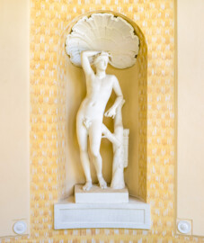 Schloss und Schlossgarten Schwetzingen - Garten - Badhaus - Von aussen - Nordseite - Vorhalle / Intrada, Westseite - Von Nordost - Blick auf die Skulptur des Apollino in einer rundbogigen Wandnische, rechts ein Stumpf eines Lorbeerbaums mit Köcher und Pfeilen, oben eine stuckierte Muschel, Wand in hellgelber Tönung mit Tropfenornamentik (Höhe 141 Zentimeter; Gipsabguß aus dem Mannheimer Antikensaal, 1980 erstellt; Original ausgestellt in den Uffizien in Florenz, 1500 in Rom ausgegraben) (aufgenommen im April 2024, um die Mittagszeit)
