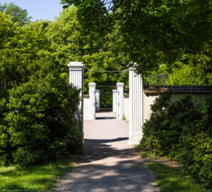 Schloss und Schlossgarten Schwetzingen - Garten - Fasanenhof - Von Osten - Blick vom südwestlichen Arboretum (Sektor F) auf die beiden Torpfosten des östlichen Tors zum ummauerten Fasanenhof mit den beiden Bruthäusern; hinter den mittleren Torpfosten liegt der Vorplatz bzw. Durchgang zwischen den Wasserspeienden Vögeln und dem Perspektiv; an den Torpfosten des Fasanenhofes waren ehemals Gittertore angebracht; der Fasanenhof war ehemals dreigeteilt: in der Mitte ein Weg zum Vorplatz (bzw. zum Apollokanal), rechts und links davon durch Gitter zur Seite und durch Netze nach oben geschlossene Gehege; gezüchtet wurden Fasane zum Aussetzen bei Jagden (Hof: Länge x Breite (ohne Bruthäuser) ca. 18 Meter x 14 Meter; Bauzeit: zwischen 1763 und 1767 (gleichzeitig mit der ehemaligen Menagerie); Architekt: Nicolas de Pigage) (aufgenommen im Mai 2024, am späten Vormittag)