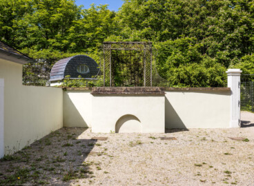 Schloss und Schlossgarten Schwetzingen - Garten - Fasanenhof - Von Osten - Blick von der südostlichen Ecke des Hofes nach Westen auf die südliche kleine Aussichtsterrasse mit dem Bogen unten (unterhalb der Bildmitte), dem Laubengang zur Terrasse (oberhalb und hinter der Terrasse), der Rückseite der nordöstlichen Voliere der Wasserspeienden Vögel (links des Laubengangs), dem südlichen Fasanenbruthaus (ganz links) sowie auf einen der beiden westlichen Torpfosten des Hofes (ganz rechts); gezüchtet wurden Fasane zum Aussetzen bei Jagden (Hof: Länge x Breite (ohne Bruthäuser) ca. 18 Meter x 14 Meter; Bauzeit: zwischen 1763 und 1767 (gleichzeitig mit der ehemaligen Menagerie); Architekt: Nicolas de Pigage) (aufgenommen im Mai 2024, am späten Vormittag) Schloss und Schlossgarten Schwetzingen - Garten - Fasanenhof - Von Osten - Blick von der südostlichen Ecke des Hofes nach Westen auf die südliche kleine Aussichtsterrasse mit dem Bogen unten (unterhalb der Bildmitte), dem Laubengang zur Terrasse (oberhalb und hinter der Terrasse), der Rückseite der nordöstlichen Voliere der Wasserspeienden Vögel (links des Laubengangs), dem südlichen Fasanenbruthaus (ganz links) sowie auf einen der beiden westlichen Torpfosten des Hofes (ganz rechts); gezüchtet wurden Fasane zum Aussetzen bei Jagden (Hof: Länge x Breite (ohne Bruthäuser) ca. 18 Meter x 14 Meter; Bauzeit: zwischen 1763 und 1767 (gleichzeitig mit der ehemaligen Menagerie); Architekt: Nicolas de Pigage) (aufgenommen im Mai 2024, am späten Vormittag)