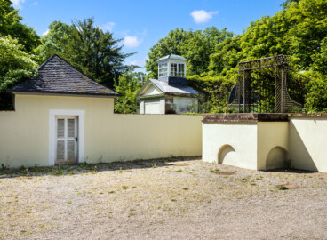 Schloss und Schlossgarten Schwetzingen - Garten - Fasanenhof - Von Nordost - Blick von der Mitte des Fasanenhofs nach Südwesten auf den Hof, das südliche Fasanenbruthaus (links), die südliche kleine Aussichtsterrasse mit den beiden Bögen unten (rechts), der Laubengang zur Terrasse (darüber) sowie auf das östliche Achathäuschen mit der Laterne der Wasserspeienden Vögel (in der Bildmitte); gezüchtet wurden Fasane zum Aussetzen bei Jagden (Hof: Länge x Breite (ohne Bruthäuser) ca. 18 Meter x 14 Meter; Bauzeit: zwischen 1763 und 1767 (gleichzeitig mit der ehemaligen Menagerie); Architekt: Nicolas de Pigage) (aufgenommen im Mai 2024, um die Mittagszeit)
