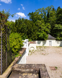 Schloss und Schlossgarten Schwetzingen - Garten - Fasanenhof - Von Süden - Blick von der südlichen kleinen Aussichtsterrasse (unten) auf die nördliche Terrasse (in der Bildmitte), auf den Abschluss des Laubengangs zur Terrasse (ganz links), auf die beiden westlichen Torpfosten des Hofs (links der Bildmitte) sowie auf das nördliche Fasanenbruthaus (rechts hinten); der Fasanenhof war ehemals dreigeteilt: in der Mitte ein Weg zum Apollokanal (nach links) und zum Arboretum (nach rechts), davor und dahinter durch Gitter und durch Netze nach oben geschlossene Gehege; an den Torpfosten des Fasanenhofes waren ehemals Gittertore angebracht; an der nördlichen kleinen Aussichtsterrasse mit dem Bogen unten befinden sich heute noch oben an der Umfassung aus rotem Sandstein einige der Metallhaken, an denen ehemals Netze über die Gehege aufgespannt wurden; gezüchtet wurden Fasane zum Aussetzen bei Jagden (Hof: Länge x Breite (ohne Bruthäuser) ca. 18 Meter x 14 Meter; Bauzeit: zwischen 1763 und 1767 (gleichzeitig mit der ehemaligen Menagerie); Architekt: Nicolas de Pigage) (aufgenommen im Mai 2024, um die Mittagszeit) Schloss und Schlossgarten Schwetzingen - Garten - Fasanenhof - Von Süden - Blick von der südlichen kleinen Aussichtsterrasse (unten) auf die nördliche Terrasse (in der Bildmitte), auf den Abschluss des Laubengangs zur Terrasse (ganz links), auf die beiden westlichen Torpfosten des Hofs (links der Bildmitte) sowie auf das nördliche Fasanenbruthaus (rechts hinten); der Fasanenhof war ehemals dreigeteilt: in der Mitte ein Weg zum Apollokanal (nach links) und zum Arboretum (nach rechts), davor und dahinter durch Gitter und durch Netze nach oben geschlossene Gehege; an den Torpfosten des Fasanenhofes waren ehemals Gittertore angebracht; an der nördlichen kleinen Aussichtsterrasse mit dem Bogen unten befinden sich heute noch oben an der Umfassung aus rotem Sandstein einige der Metallhaken, an denen ehemals Netze über die Gehege aufgespannt wurden; gezüchtet wurden Fasane zum Aussetzen bei Jagden (Hof: Länge x Breite (ohne Bruthäuser) ca. 18 Meter x 14 Meter; Bauzeit: zwischen 1763 und 1767 (gleichzeitig mit der ehemaligen Menagerie); Architekt: Nicolas de Pigage) (aufgenommen im Mai 2024, um die Mittagszeit)