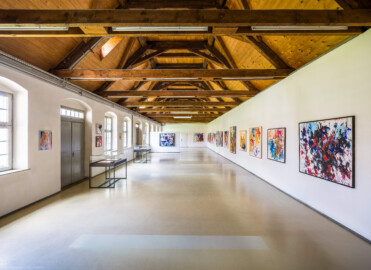 Schloss und Schlossgarten Schwetzingen - Garten - Invalidenkaserne (ehemaliges Baumagazin) / xylon - Museum + Werkstätten - Westflügel - Von innen - Von Norden - Blick nach Süden in die große Ausstellungshalle des Museums sowie nach oben in den Dachstuhl; die Türen links führen auf den Innenhof (Vierflügelanlage: Länge x Breite: ca. 60 x 50 Meter; Westflügel: ca. 50 x 10 Meter; Bauzeit: um 1774; Architekt des Baummagazins: Nicolas de Pigage; Umbau zur Kaserne: Ingenieur-Oberst von Pfister) (aufgenommen im Juni 2024, am frühen Nachmittag)
