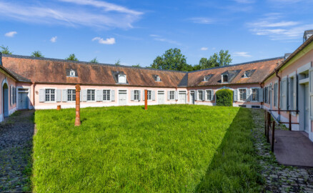 Schloss und Schlossgarten Schwetzingen - Garten - Invalidenkaserne (ehemaliges Baumagazin) - Innenhof - Von Südost - Blick von der südöstlichen Ecke des Innenhofs auf die vier Fügel der Anlage; ganz links der Westteil des Südflügels, in der Mitte der Westflügel (beide genutzt als Ausstellungsraum von xylon), rechts davon der Nordflügel (genutzt als Werkstattsraum von xylon) und ganz rechts der Ostflügel (genutzt von der Stadtbibliothek) (Vierflügelanlage: Länge x Breite: ca. 60 x 50 Meter; Südflügel: ca. 60 x 10 Meter; Bauzeit: um 1774; Architekt des Baummagazins: Nicolas de Pigage; Umbau zur Kaserne: Ingenieur-Oberst von Pfister) (aufgenommen im Juni 2024, am Vormittag)