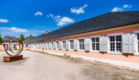 Schloss und Schlossgarten Schwetzingen - Garten - Invalidenkaserne (ehemaliges Baumagazin) - Südflügel - Von Südost - Blick vom östlichen Eingang zum Außenhof nach Nordwest auf den Südflügel der Invalidenkaserne sowie auf einen Teil des Außenhofs; die vier Fenster ganz hinten gehören zu xylon, die neun Fenster vorne gehören zur Stadtbibliothek (Vierflügelanlage: Länge x Breite: ca. 60 x 50 Meter; Südflügel: ca. 60 x 10 Meter; Bauzeit: um 1774; Architekt des Baummagazins: Nicolas de Pigage; Umbau zur Kaserne: Ingenieur-Oberst von Pfister) (aufgenommen im Juni 2024, am späten Vormittag)