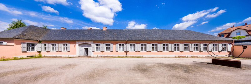 Schloss und Schlossgarten Schwetzingen - Garten - Invalidenkaserne (ehemaliges Baumagazin) - Südflügel - Von Süden - Blick vom Baumagazin (mit der Gartengeräte-Ausstellung) nach Norden auf den Südflügel der Invalidenkaserne sowie auf einen Teil des Außenhofs; die vier Fenster ganz links gehören zu xylon, die neun Fenster ganz rechts gehören zur Stadtbibliothek (Vierflügelanlage: Länge x Breite: ca. 60 x 50 Meter; Südflügel: ca. 60 x 10 Meter; Bauzeit: um 1774; Architekt des Baummagazins: Nicolas de Pigage; Umbau zur Kaserne: Ingenieur-Oberst von Pfister) (aufgenommen im Juni 2024, um die Mittagszeit)