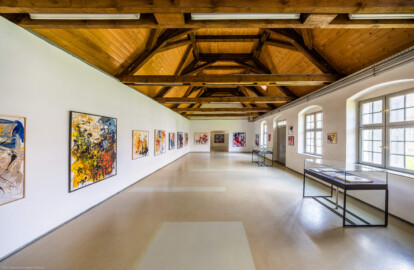 Schloss und Schlossgarten Schwetzingen - Garten - Invalidenkaserne (ehemaliges Baumagazin) / xylon - Museum + Werkstätten - Westflügel - Von innen - Von Süden - Blick nach Norden in einen Teil der großen Ausstellungshalle des Museums sowie nach oben in den Dachstuhl; hinter der Tür und den Fenstern rechts liegt der Innenhof (Vierflügelanlage: Länge x Breite: ca. 60 x 50 Meter; Westflügel: ca. 50 x 10 Meter; Bauzeit: um 1774; Architekt des Baummagazins: Nicolas de Pigage; Umbau zur Kaserne: Ingenieur-Oberst von Pfister) (aufgenommen im Juni 2024, am frühen Nachmittag)